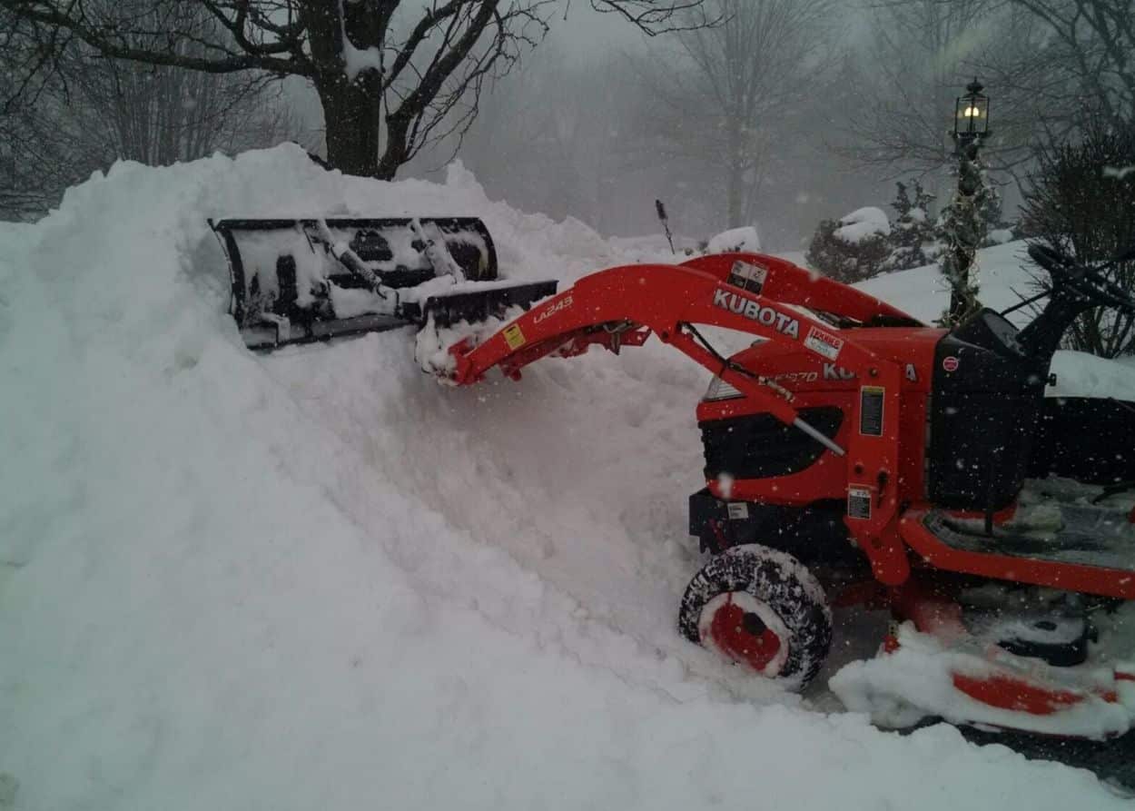 Snow pusher in action on tractor, plowing snow into one big pile.